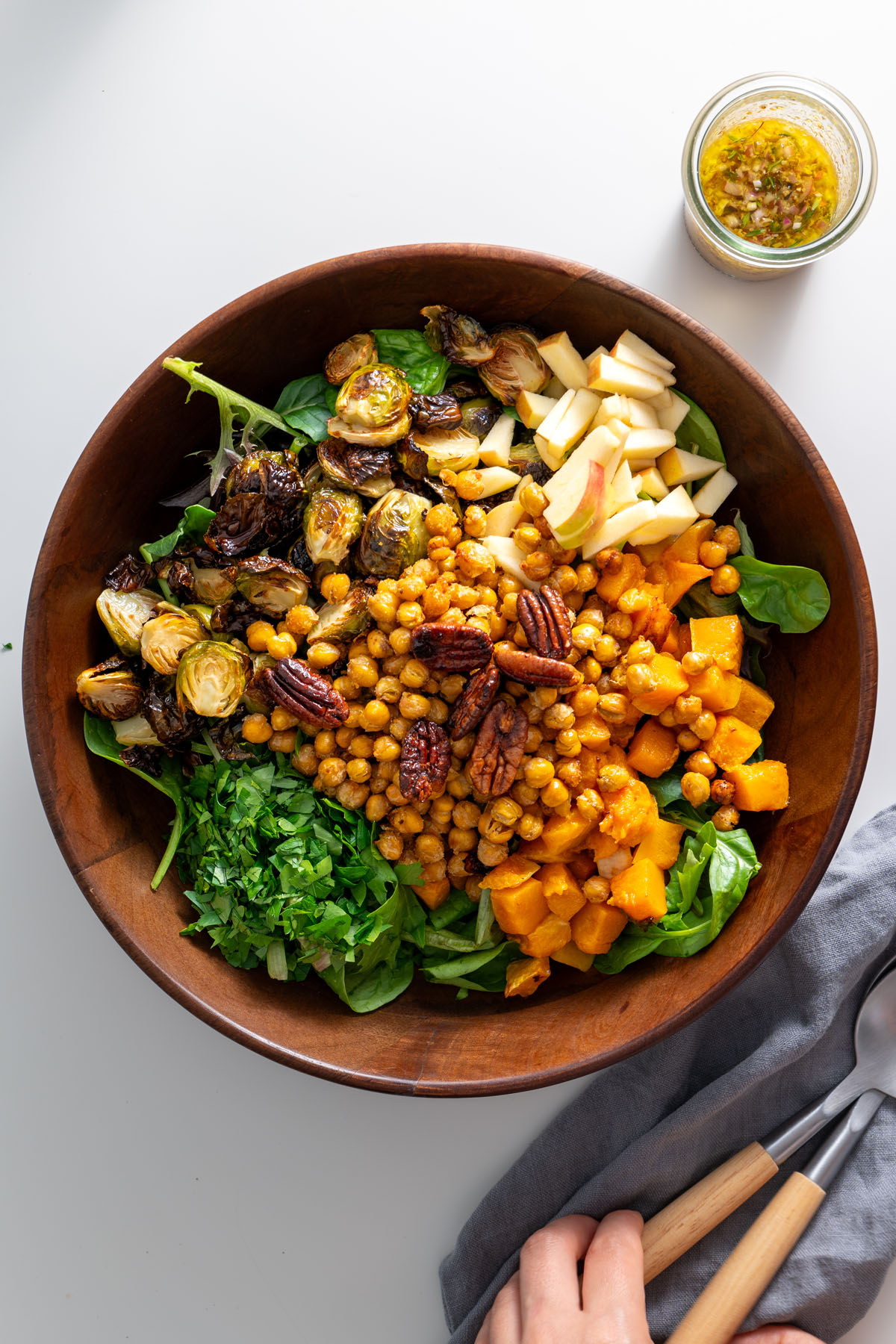 Bright and fresh ingredients for a fall salad, including chopped apples, roasted butternut squash, and chickpeas, in a wooden bowl.