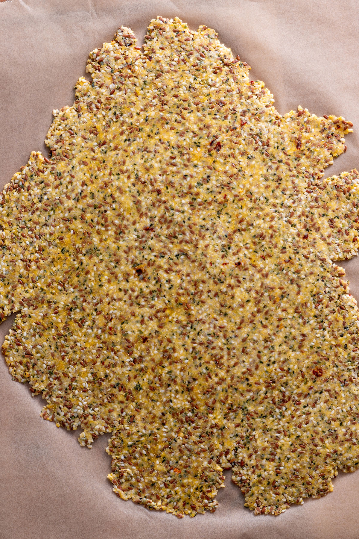 Unbaked seeded cracker dough spread on parchment paper.