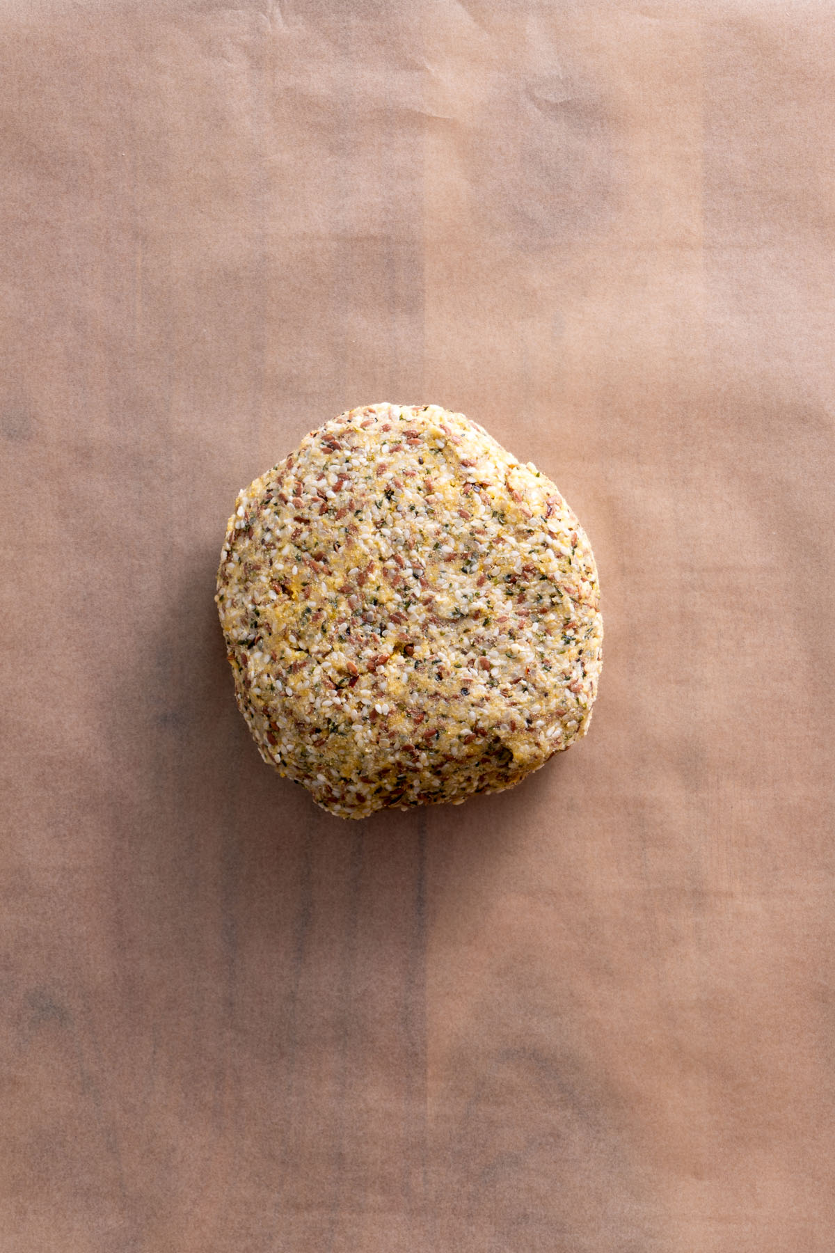 A round ball of seeded cracker dough on parchment paper.