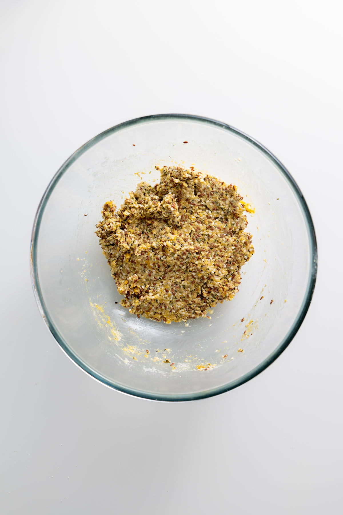Seeded cracker dough mixture in a clear mixing bowl on a white surface.