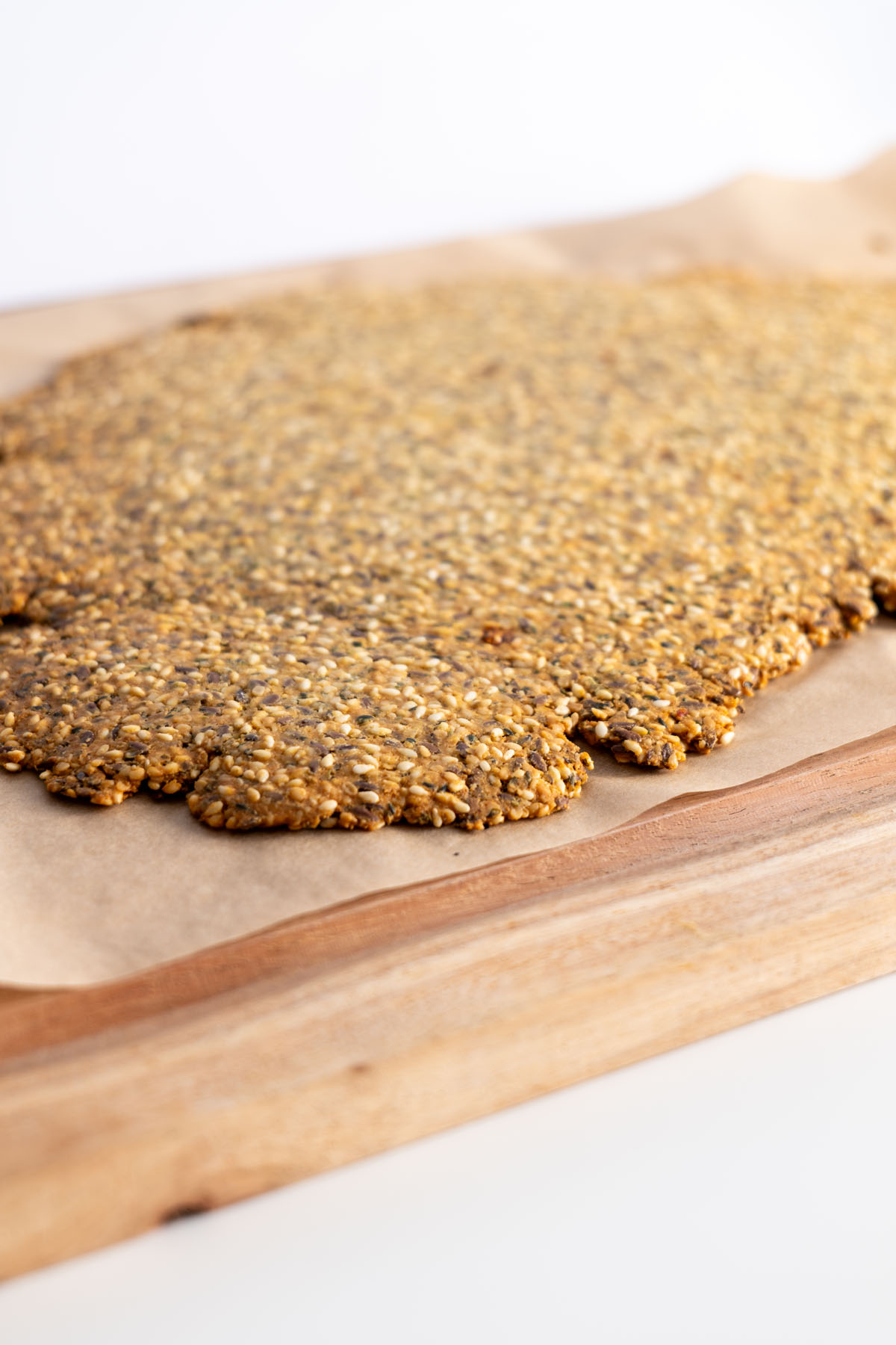 Close-up of baked healthy seeded cracker sheet on parchment paper over a wooden board.