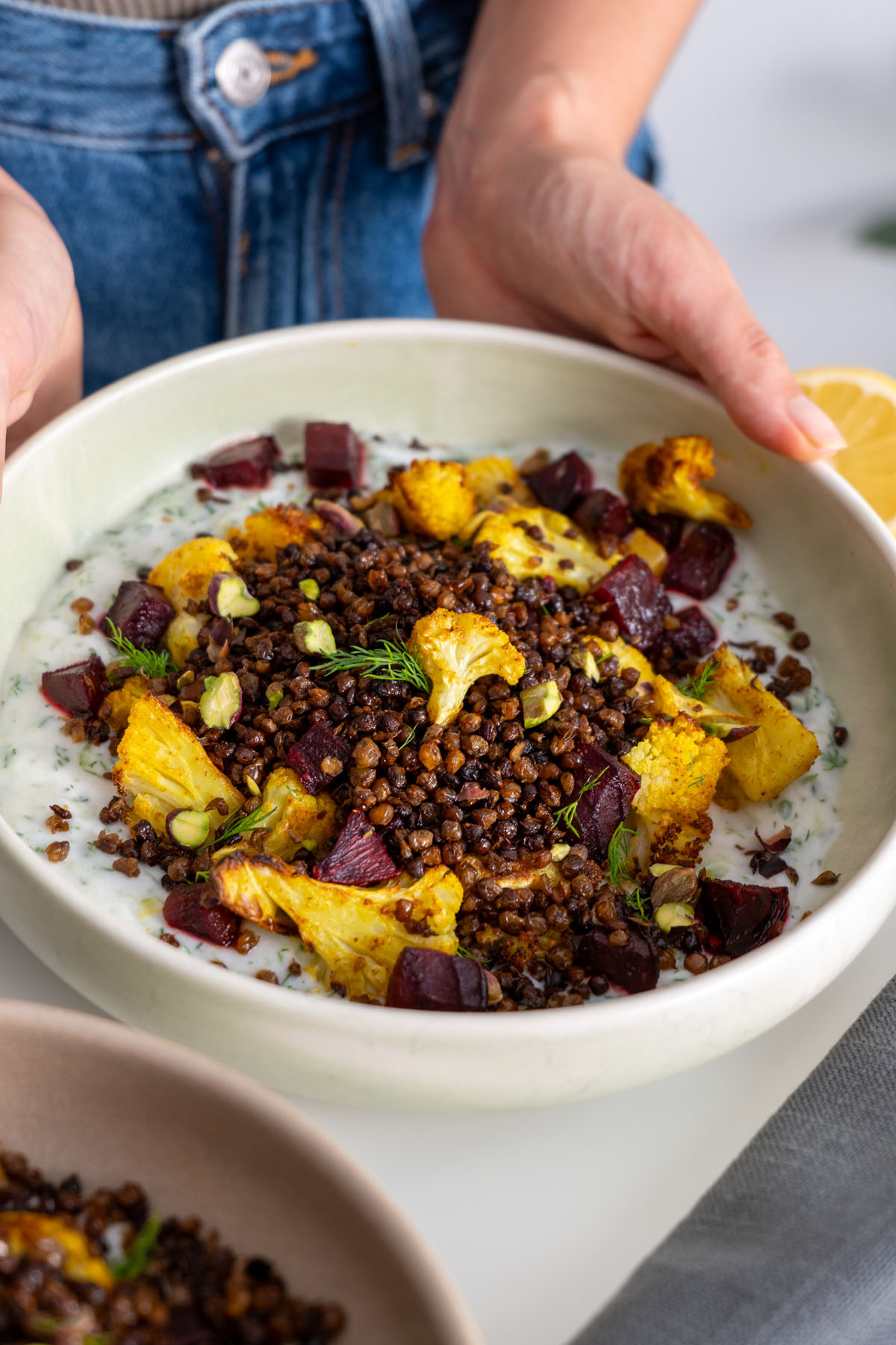 Overhead shot of a roasted cauliflower bowl with tzatziki and lentils next to cut beetroot and lemon slices.