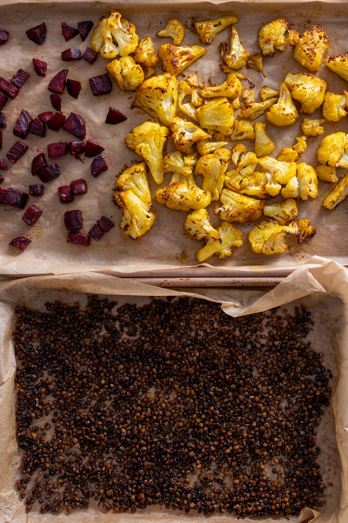 Roasted cauliflower, beetroot, and crispy lentils laid out on separate baking trays.