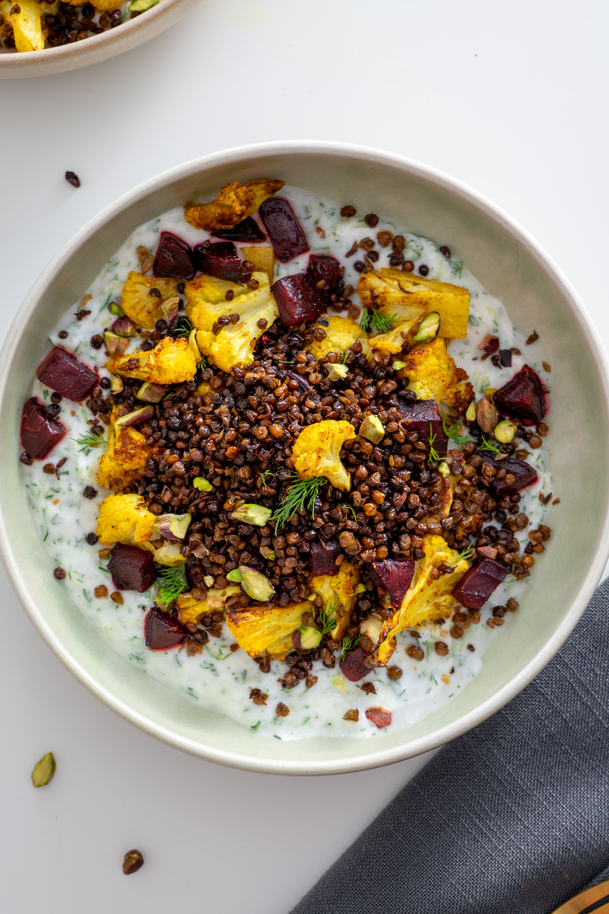 Close-up of roasted cauliflower, crispy lentils, and beetroot on a creamy tzatziki base in a green bowl.