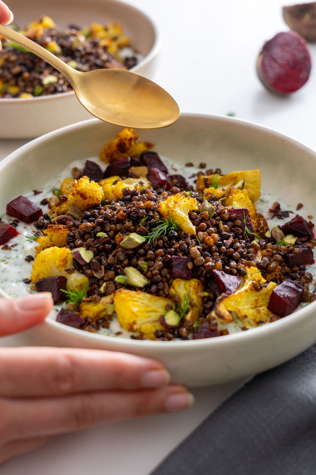 Sarah Cobacho assembling a roasted cauliflower bowl with a spoon over crispy lentils.