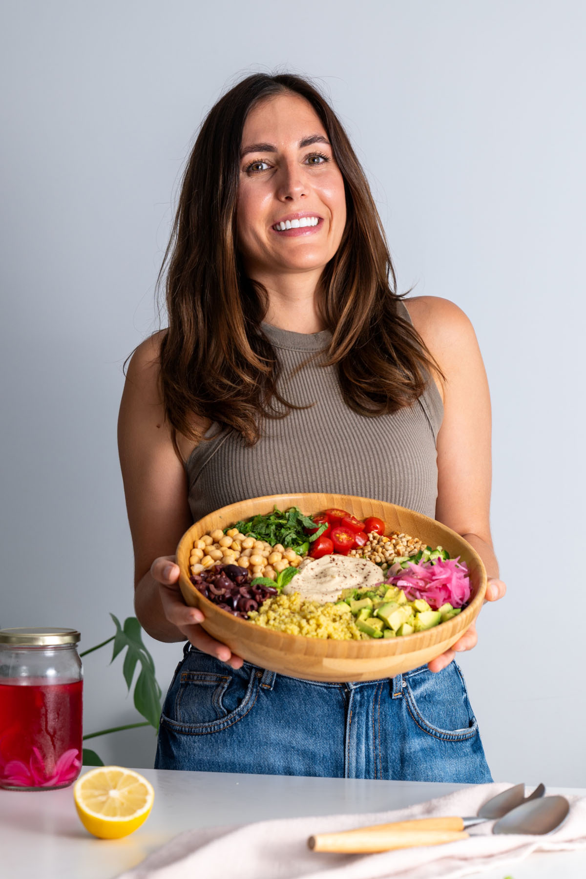 Sarah Cobacho holding a wooden bowl filled with a vibrant Mediterranean salad featuring quinoa, chickpeas, and fresh vegetables.