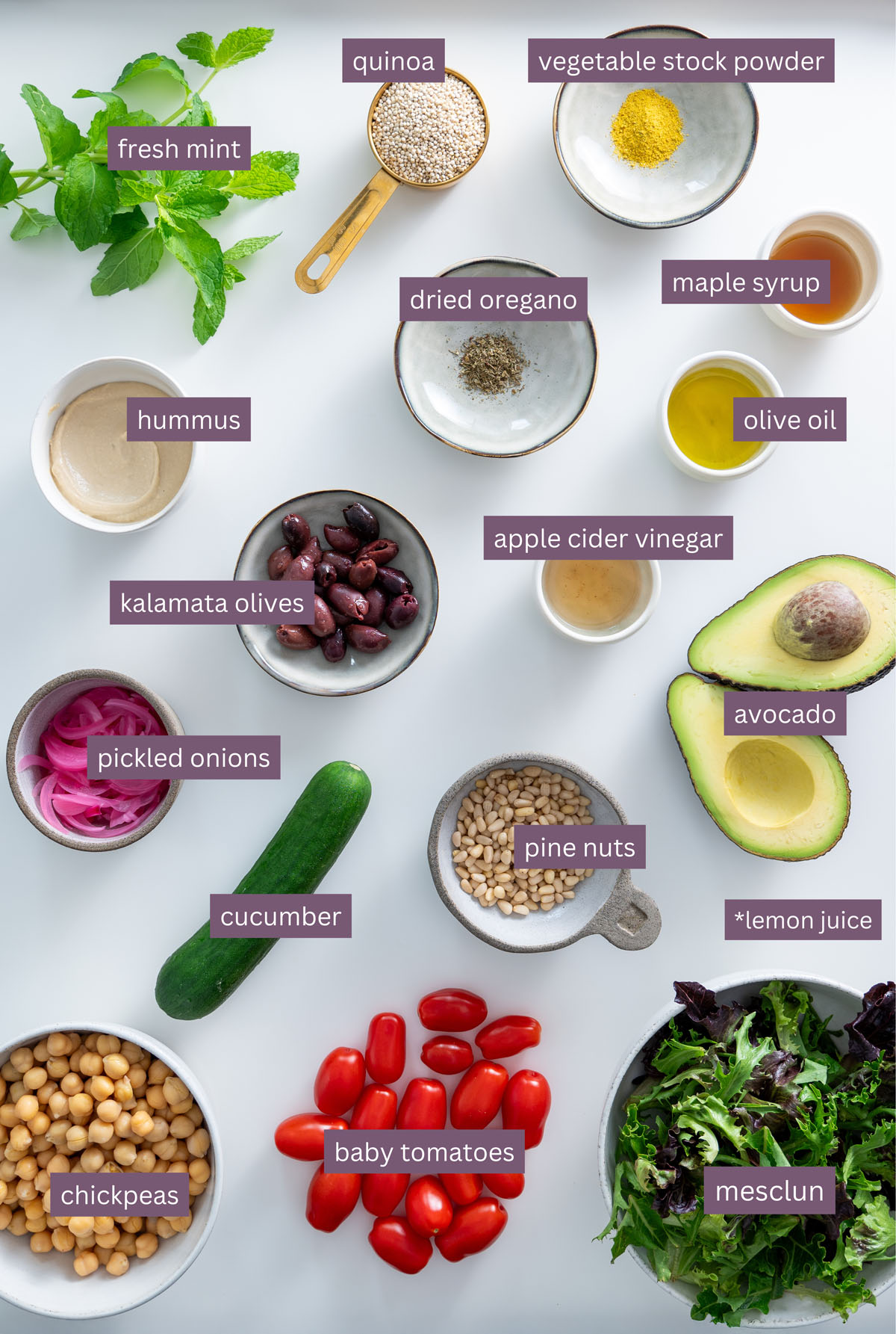 Flat lay of vibrant ingredients for a Mediterranean salad, including quinoa, hummus, chickpeas, and fresh vegetables on a white surface.