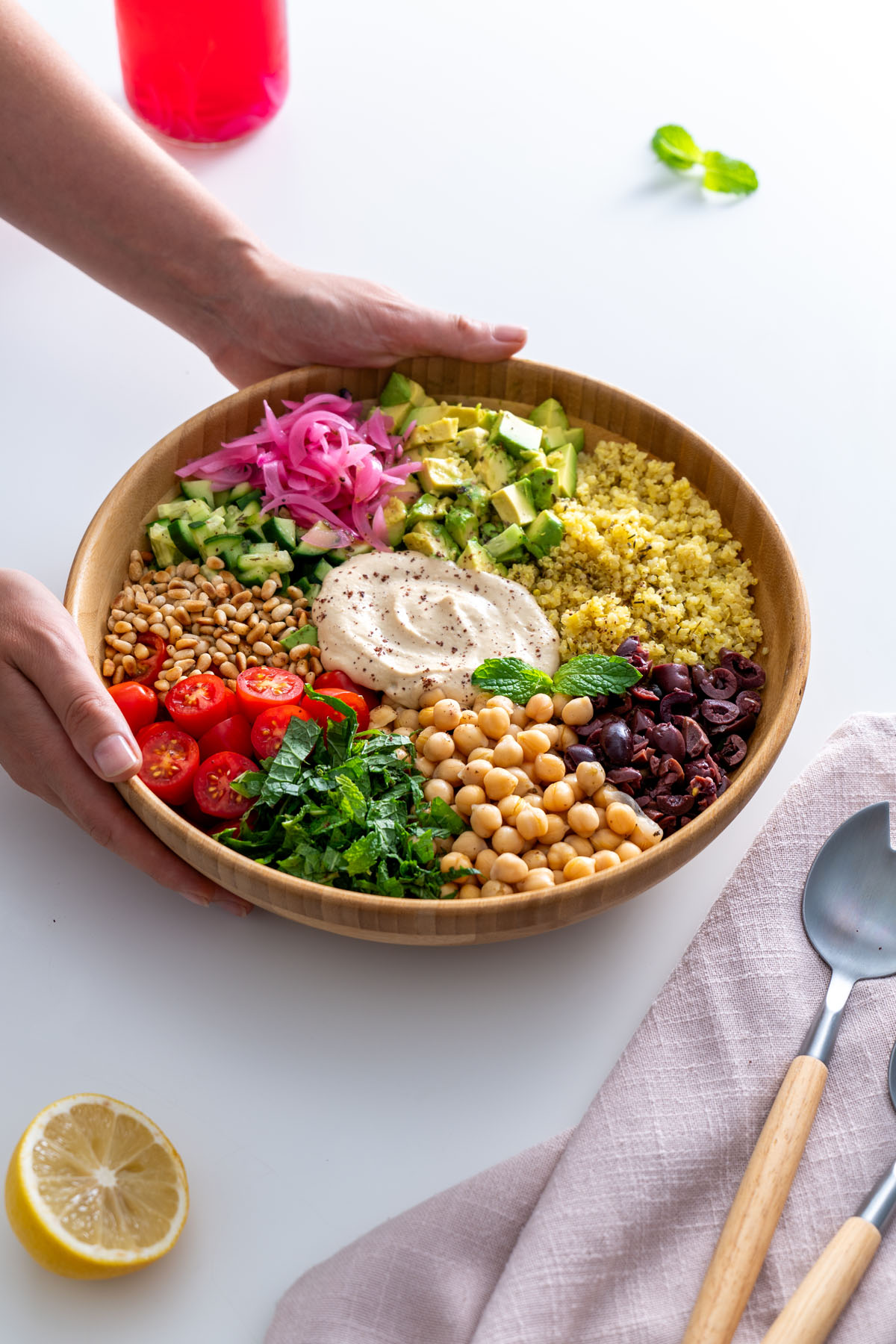 Vibrant Mediterranean salad served in a wooden bowl, garnished with fresh mint and surrounded by a napkin, lemon, and serving utensils.