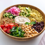 Overhead view of a Mediterranean salad with quinoa, chickpeas, and colorful fresh vegetables arranged beautifully in a wooden bowl.