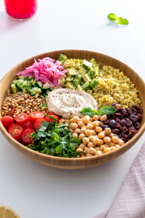 Overhead view of a Mediterranean salad with quinoa, chickpeas, and colorful fresh vegetables arranged beautifully in a wooden bowl.