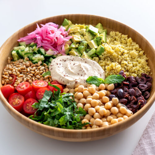 Overhead view of a Mediterranean salad with quinoa, chickpeas, and colorful fresh vegetables arranged beautifully in a wooden bowl.