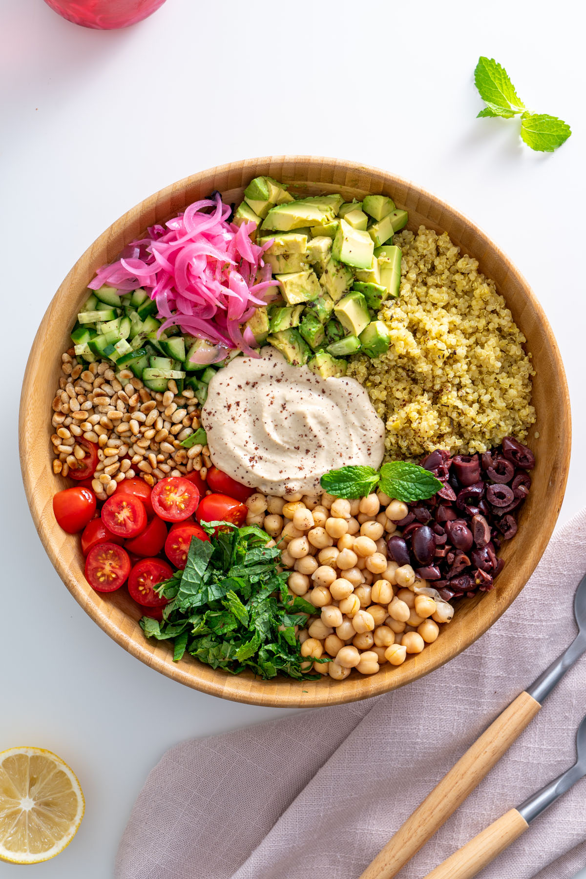 Overhead view of a Mediterranean salad with vibrant ingredients, including pickled onions, avocado, and fresh mint, on a white table.