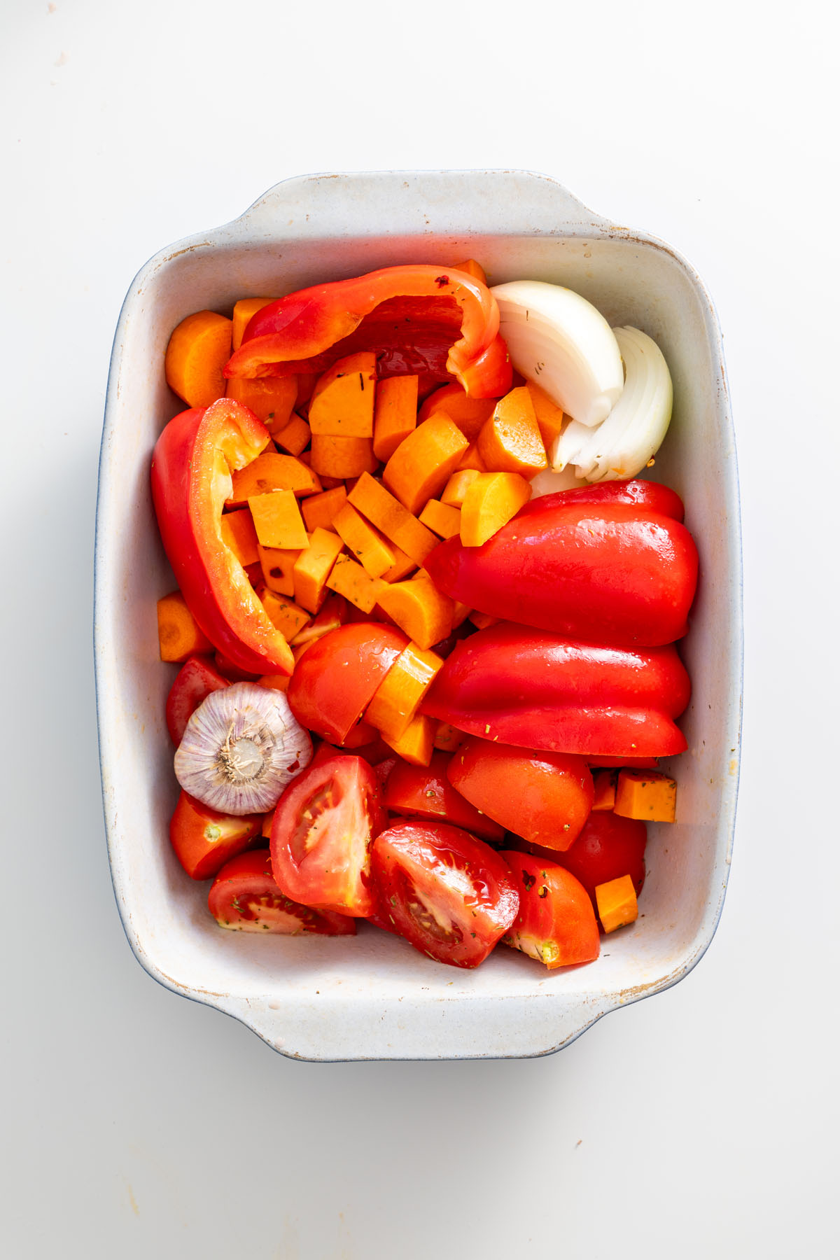 Prepared vegetables with garlic, sweet potatoes, and peppers in a baking dish.