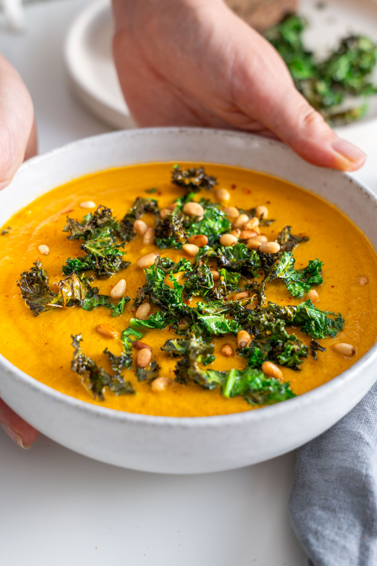 Close-up of roasted vegetable soup garnished with crispy kale and pine nuts.