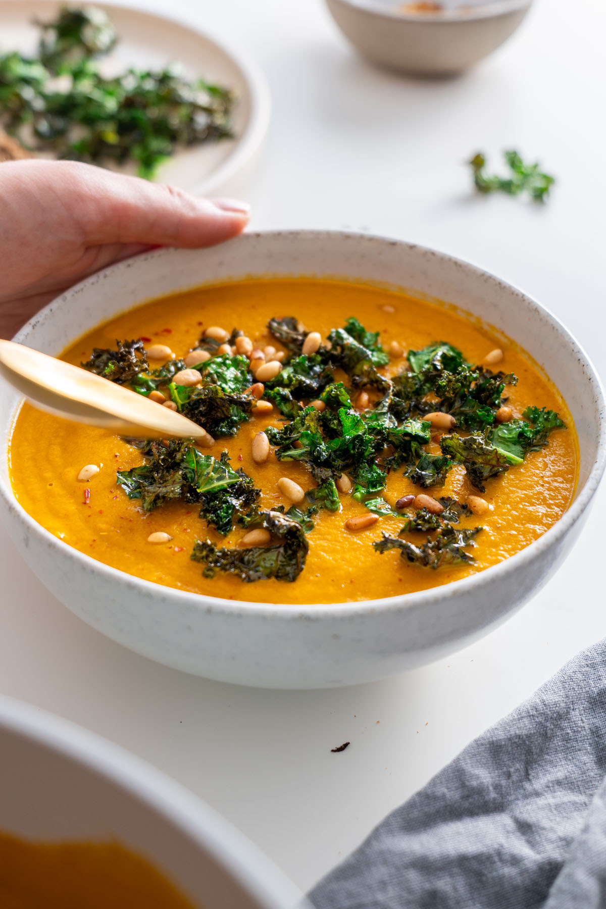 Close-up of roasted vegetable soup garnished with crispy kale and pine nuts.