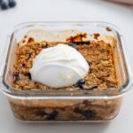 Close-up of baked blueberry oats topped with a dollop of coconut yogurt and lemon zest.