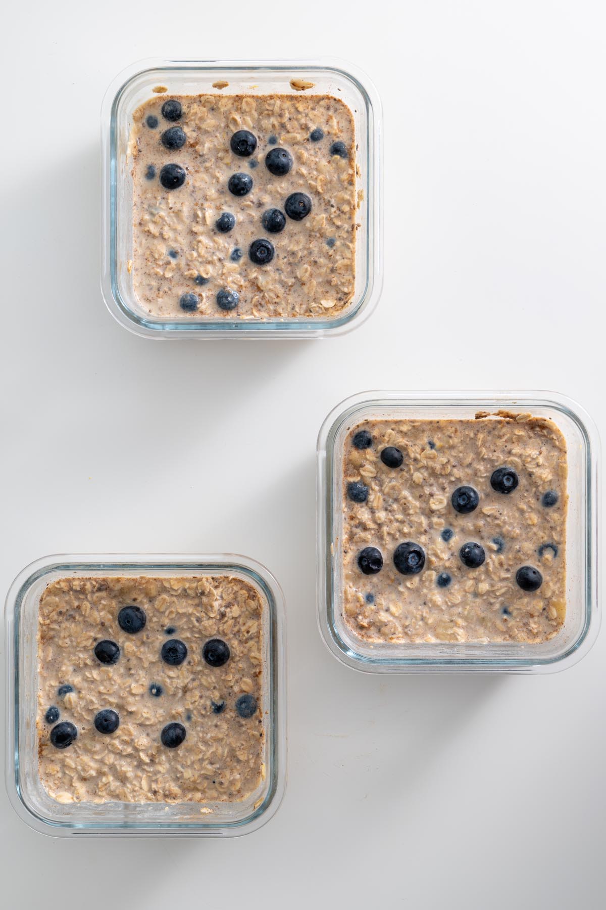 Three glass containers filled with unbaked blueberry oats, ready to go into the oven.
