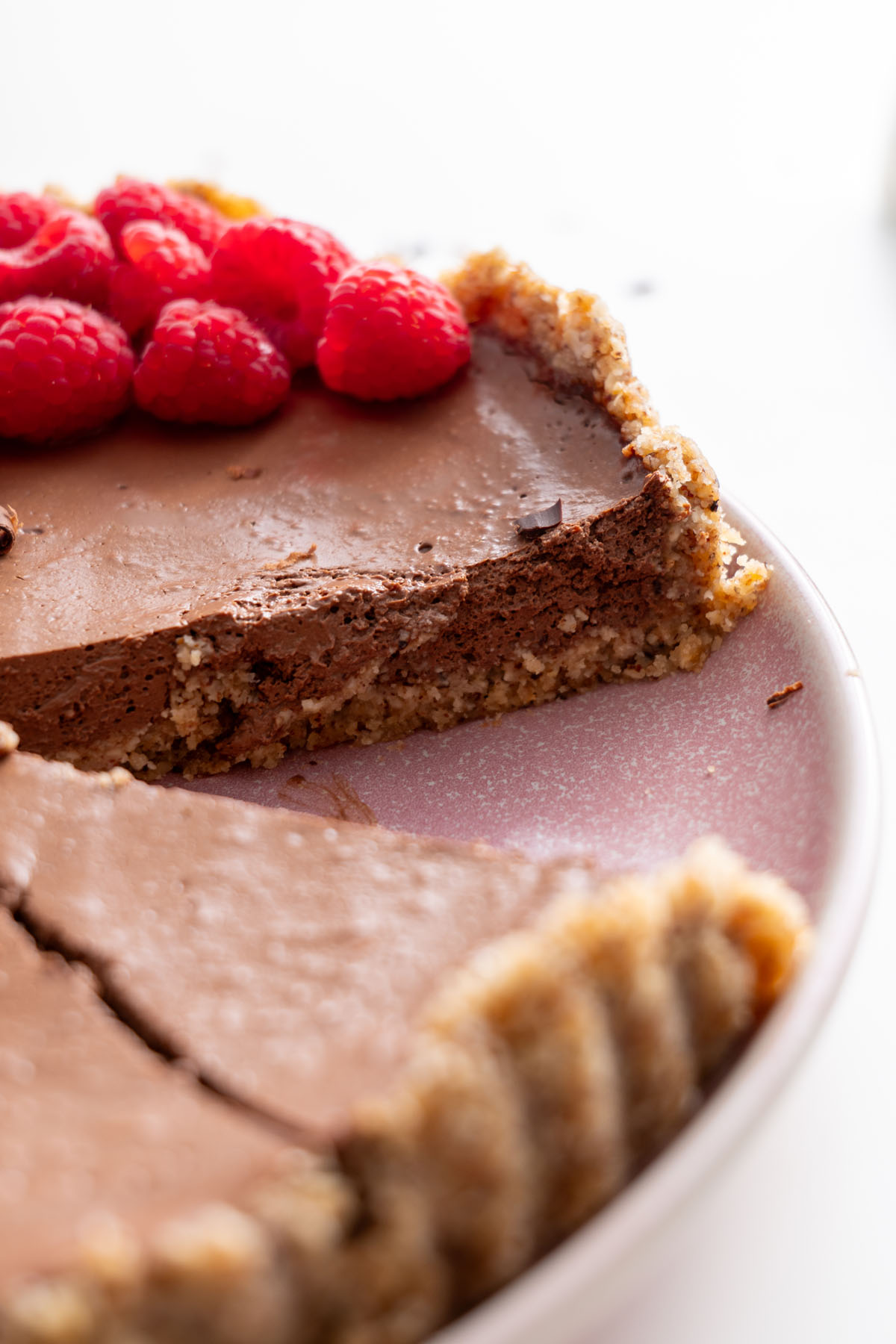 A close-up of a single slice of no-bake chocolate tart with raspberries, highlighting the smooth texture and nutty crust.