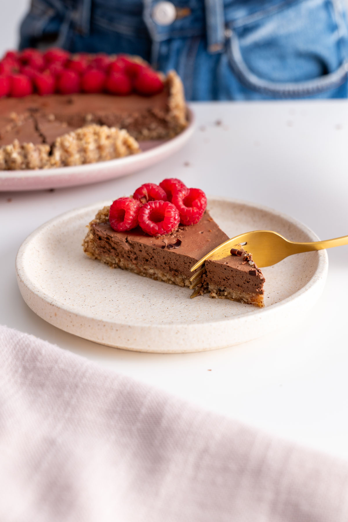A fork cutting into a slice of no-bake silken chocolate tart with raspberries on top, showing the creamy texture and nutty crust.