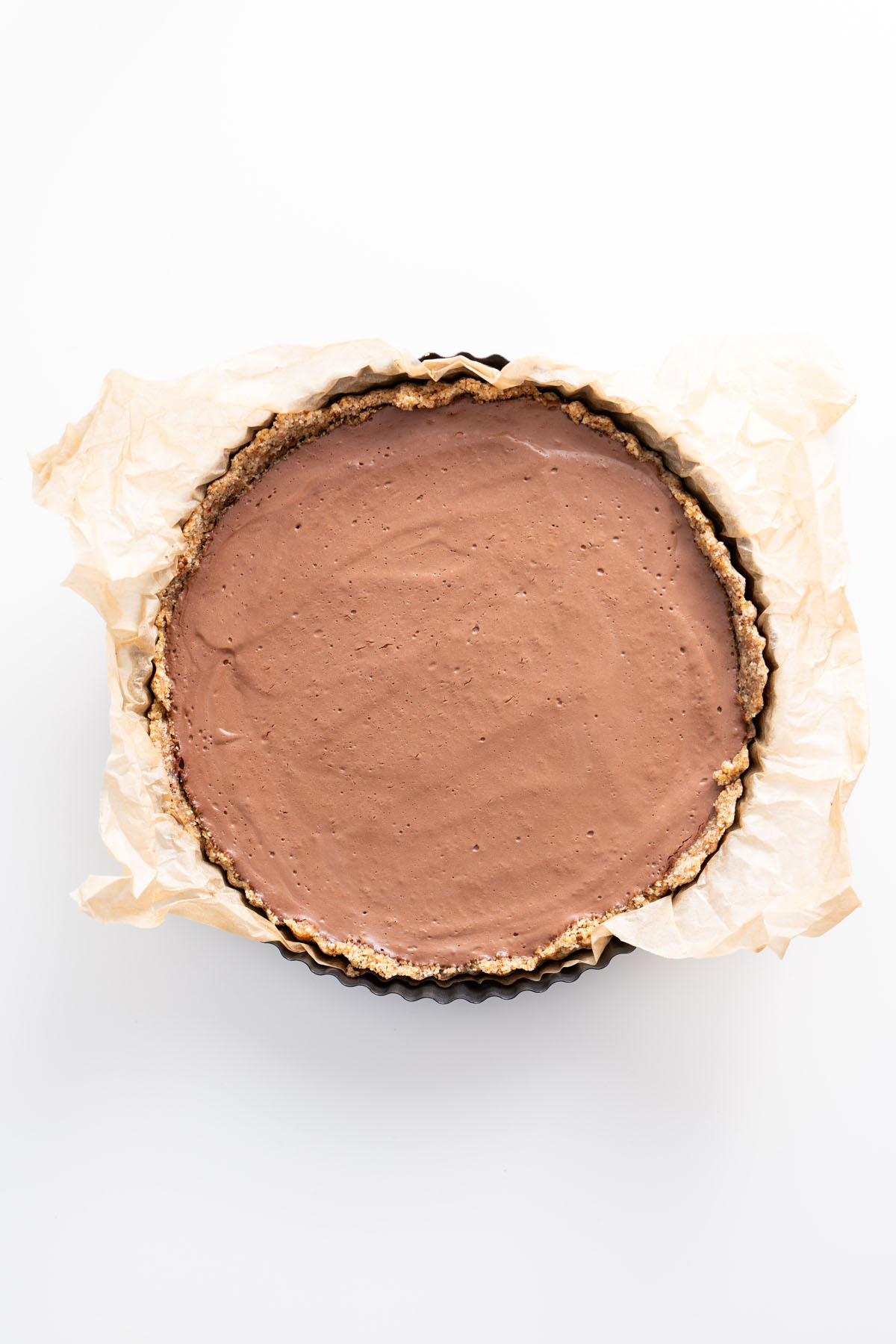 Freshly set no-bake silken chocolate tart in a parchment-lined tart pan, ready for decoration.