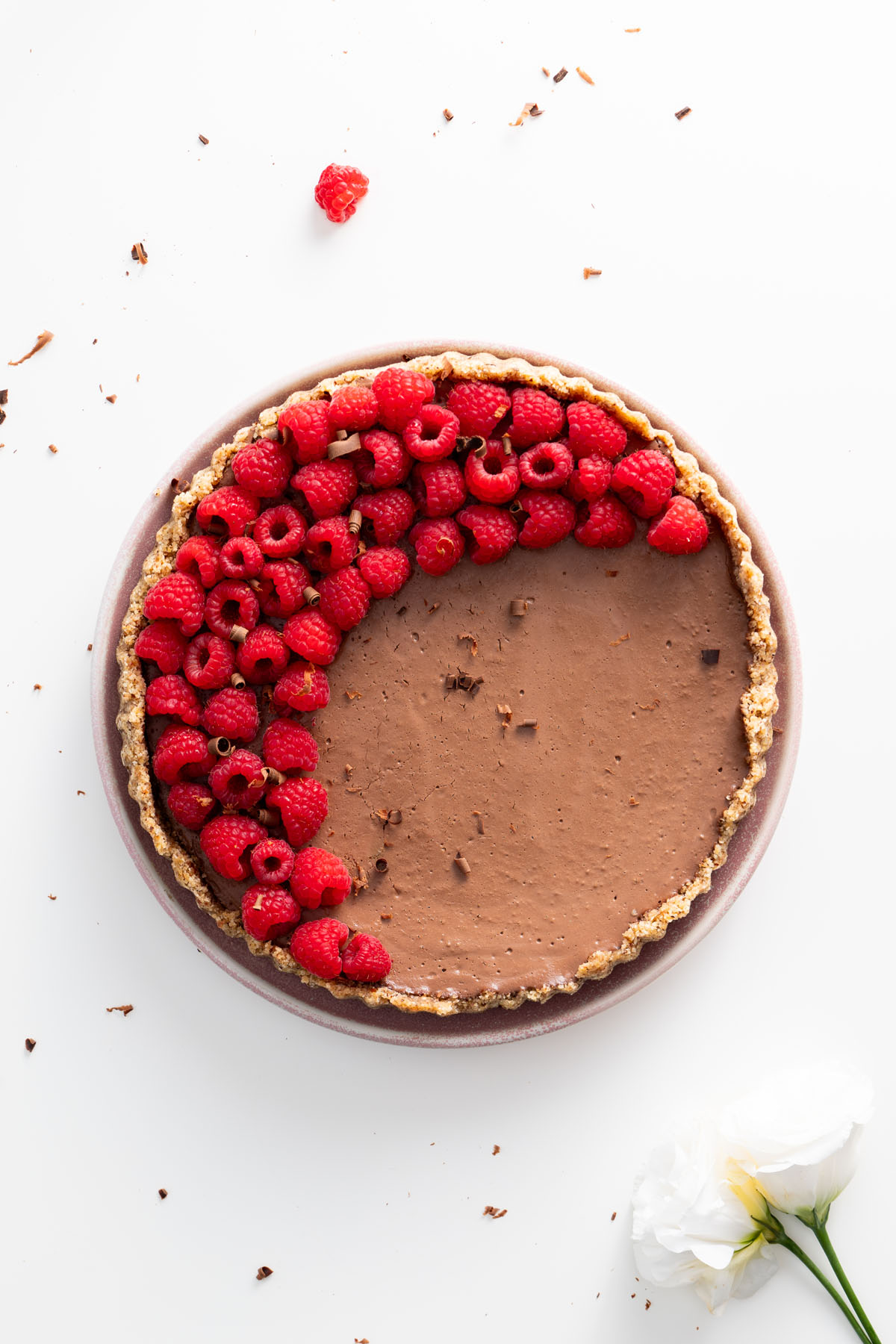 A beautifully decorated no-bake silken chocolate tart with a half-circle of vibrant raspberries and chocolate shavings on a white plate.