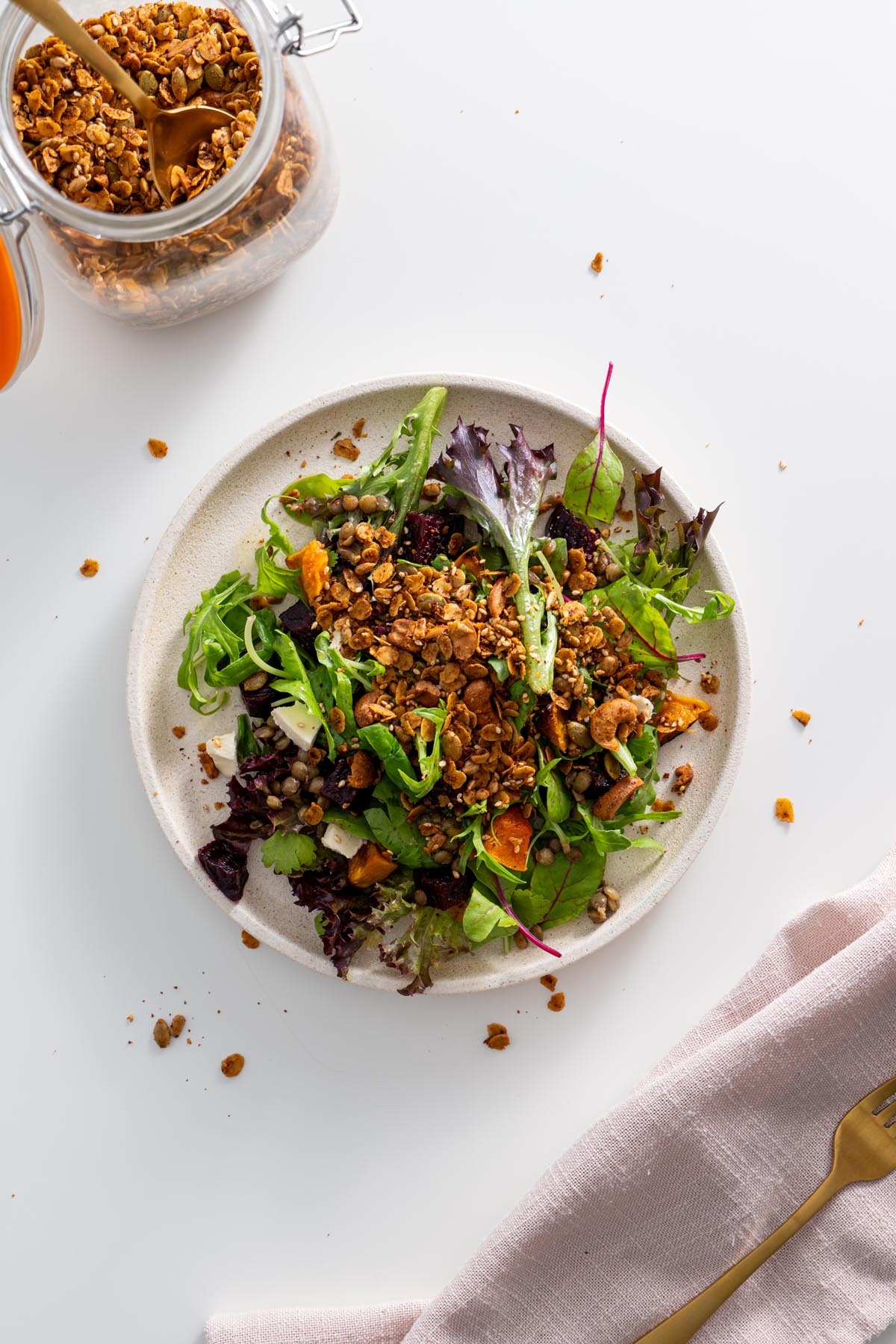 A vibrant salad topped with crunchy homemade savory granola, served on a white plate.