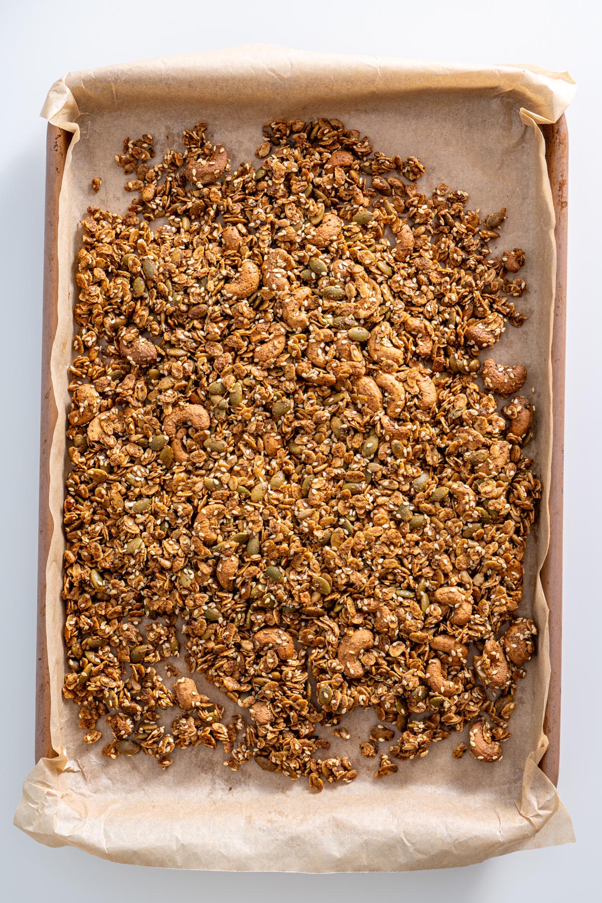 A fresh batch of homemade savory granola spread out on a parchment-lined baking tray.