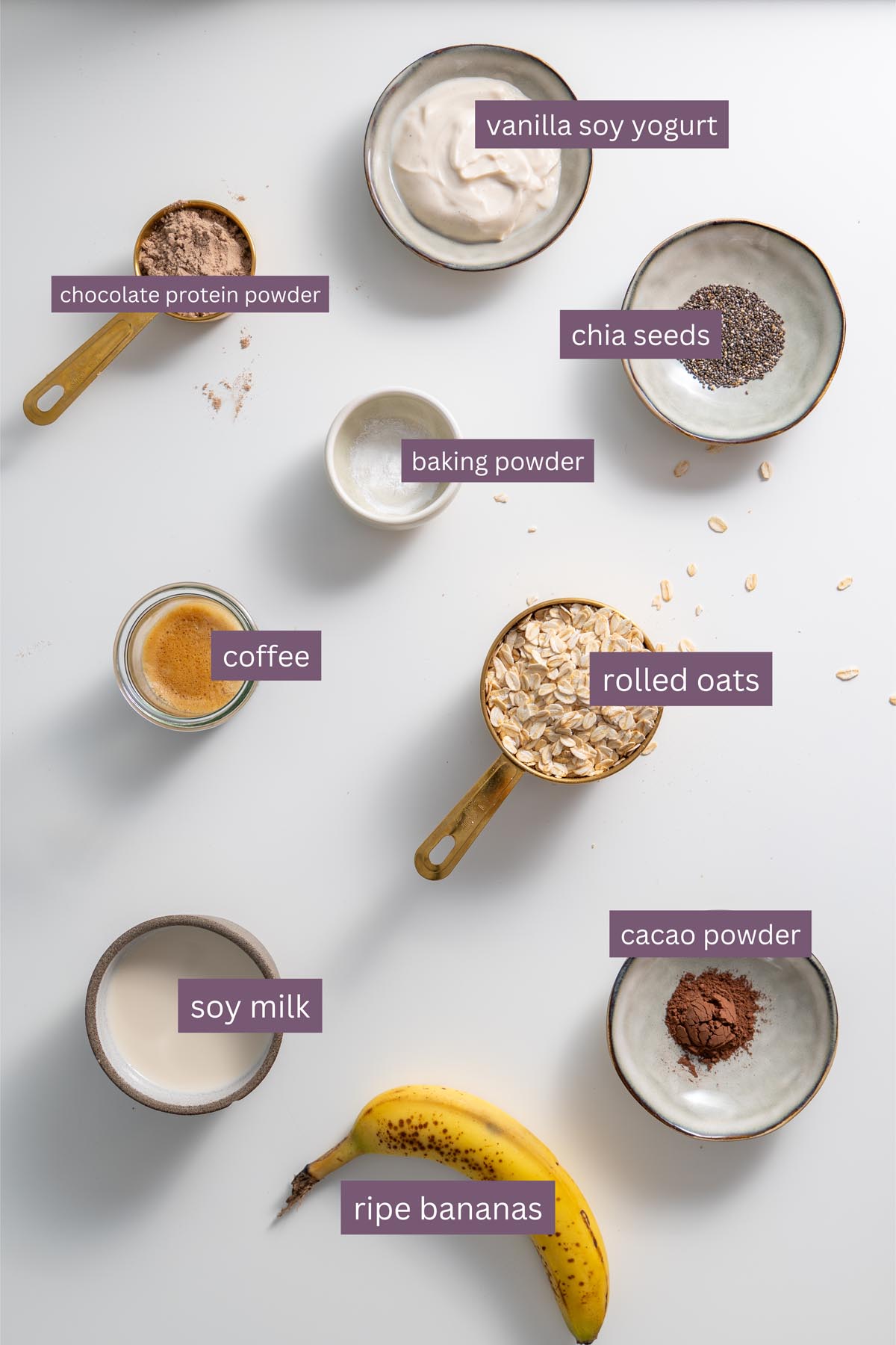 Flat lay of ingredients for tiramisu baked oats, including oats, bananas, soy milk, protein powder, and coffee on a white background