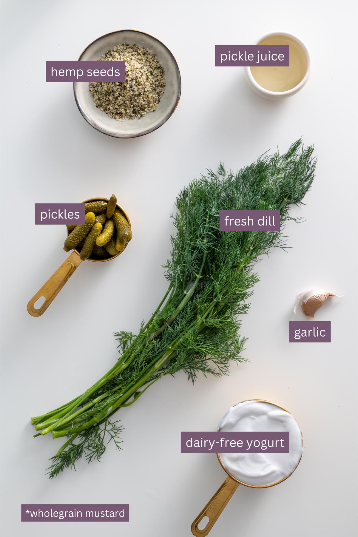 Vibrant ingredients for a creamy dill pickle dressing on a white surface, including fresh dill, hemp seeds, garlic, pickles, and yogurt.