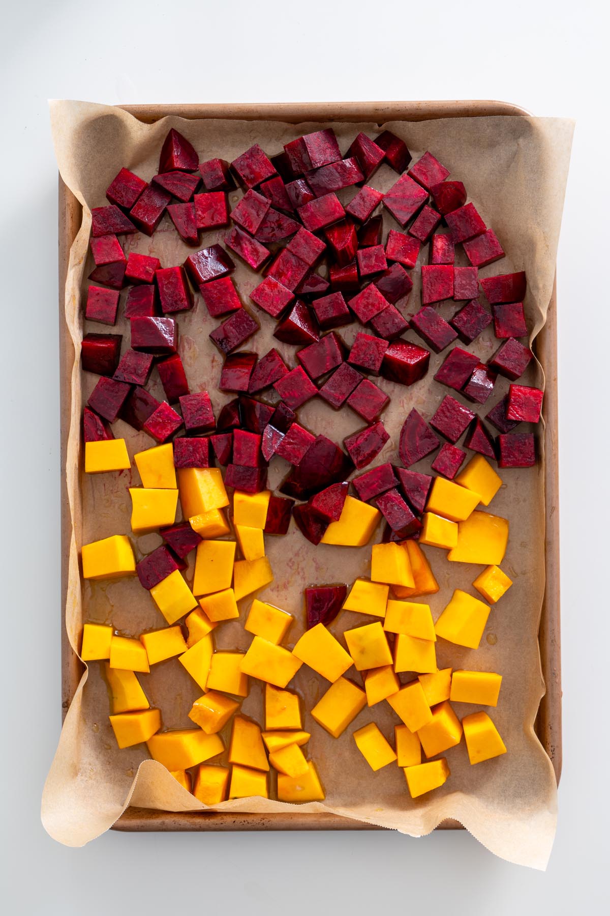Raw beetroot and pumpkin cubes spread on a parchment-lined baking sheet before roasting.