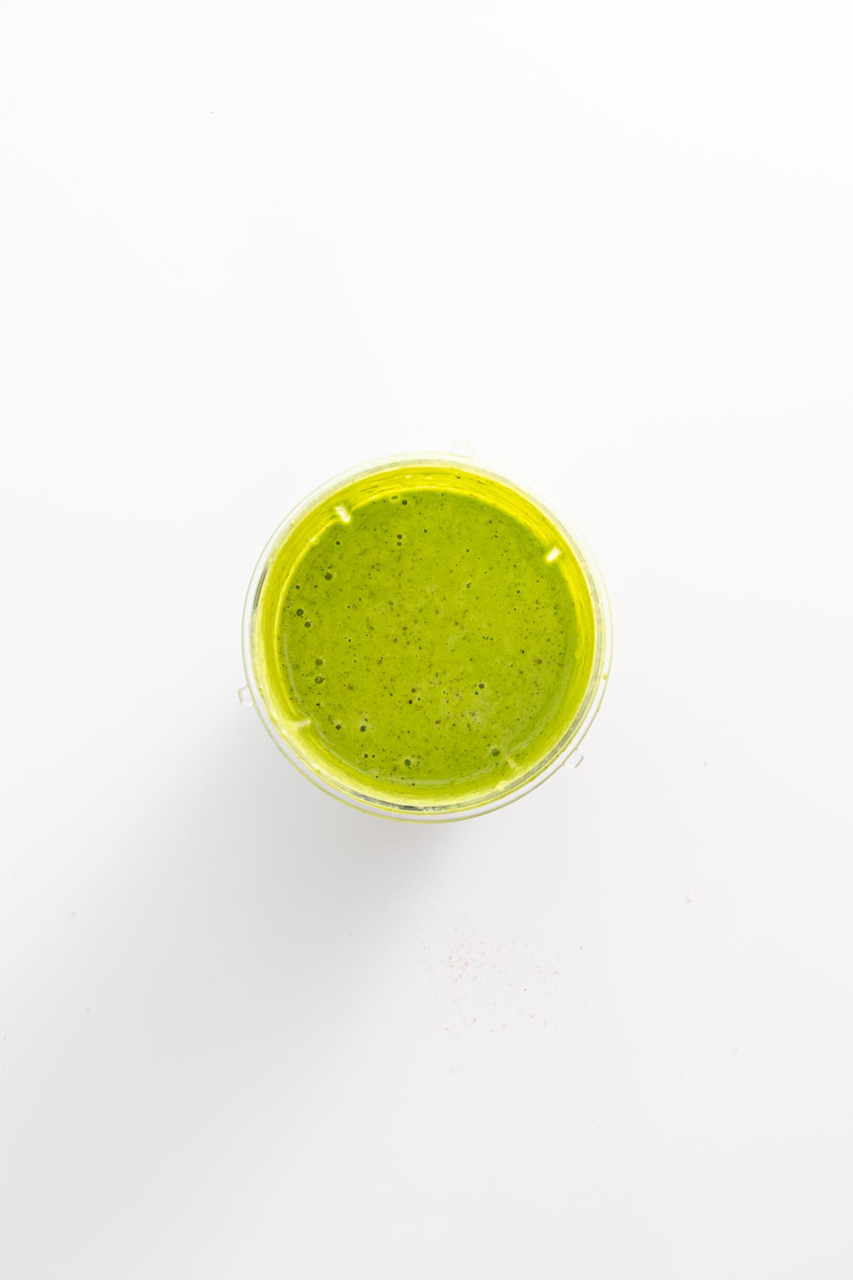 Bright green dill pickle salad dressing in a blender cup on a white background.