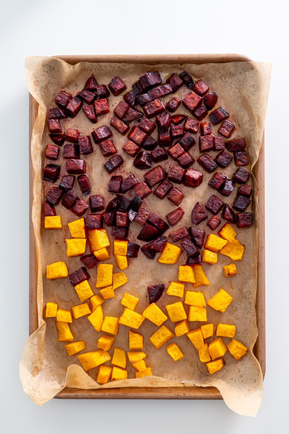 Roasted beetroot and pumpkin on a parchment-lined baking sheet, showing deep caramelized color.