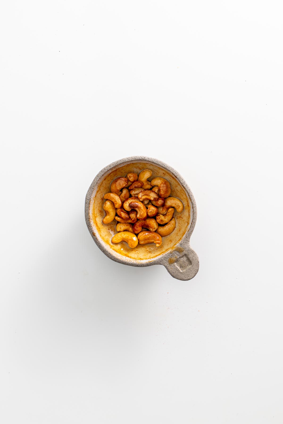 Candied cashews in a small dish, coated in maple syrup and chili powder.