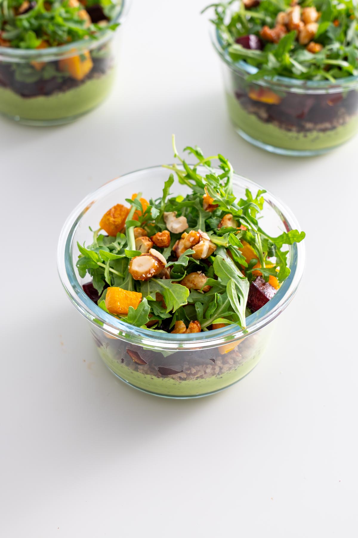 Glass meal prep containers filled with dill pickle salad, topped with arugula and candied cashews.