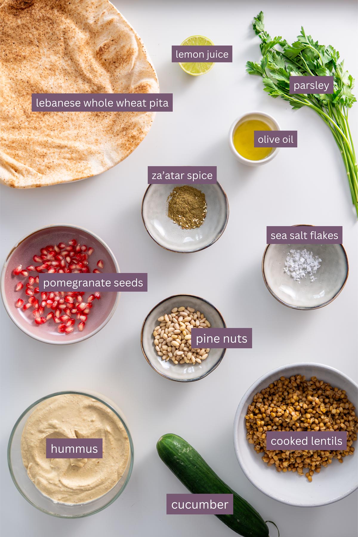 Vibrant ingredients for a hummus pita bowl on a white surface, including pita bread, hummus, lentils, and spices.