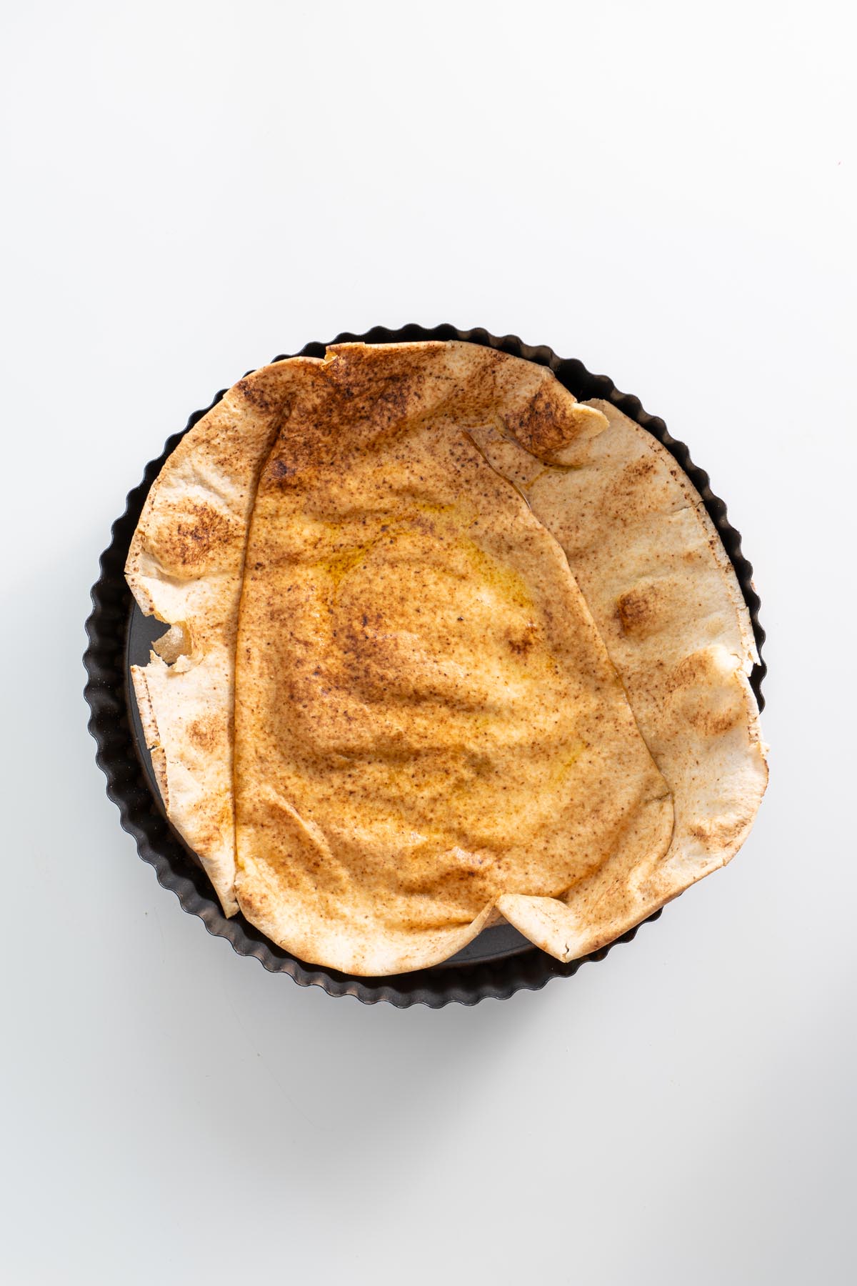 A toasted whole wheat pita shaped into a bowl, resting in a round baking pan.