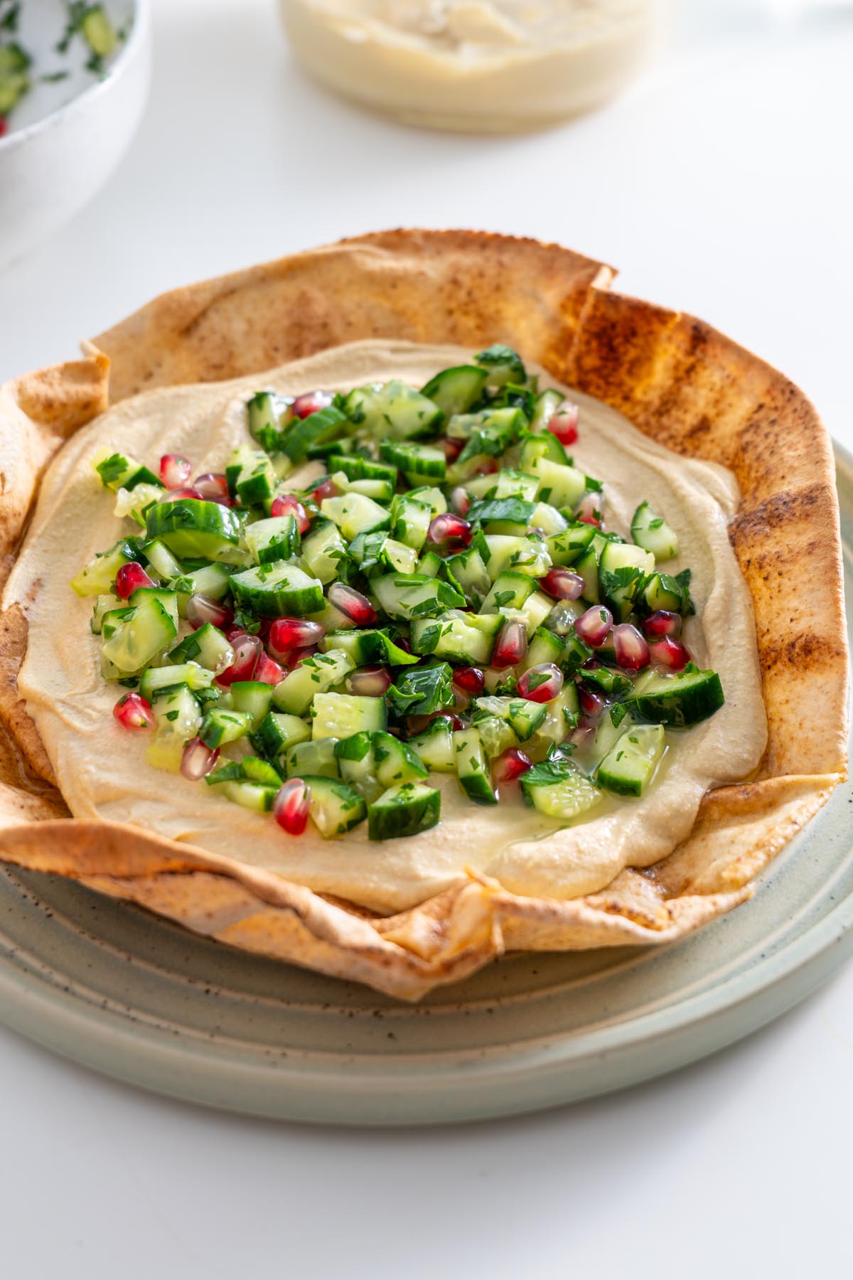 Crispy pita bowl filled with hummus and cucumber pomegranate salad, ready for assembly.