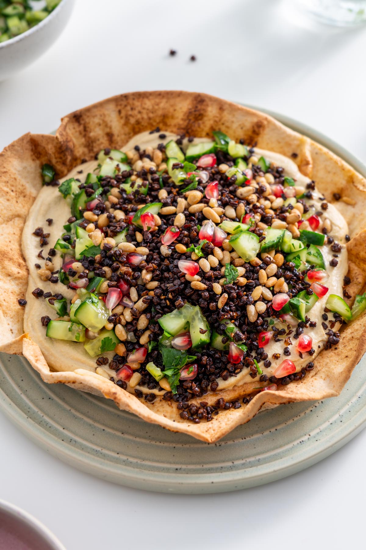 Close-up of hummus pita bowl topped with crispy lentils, pine nuts, and pomegranate seeds.