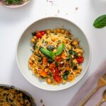 A plated bowl of Meghan Markle’s one-pot pasta on a white table with fresh arugula, chili flakes, and gold cutlery in the background.