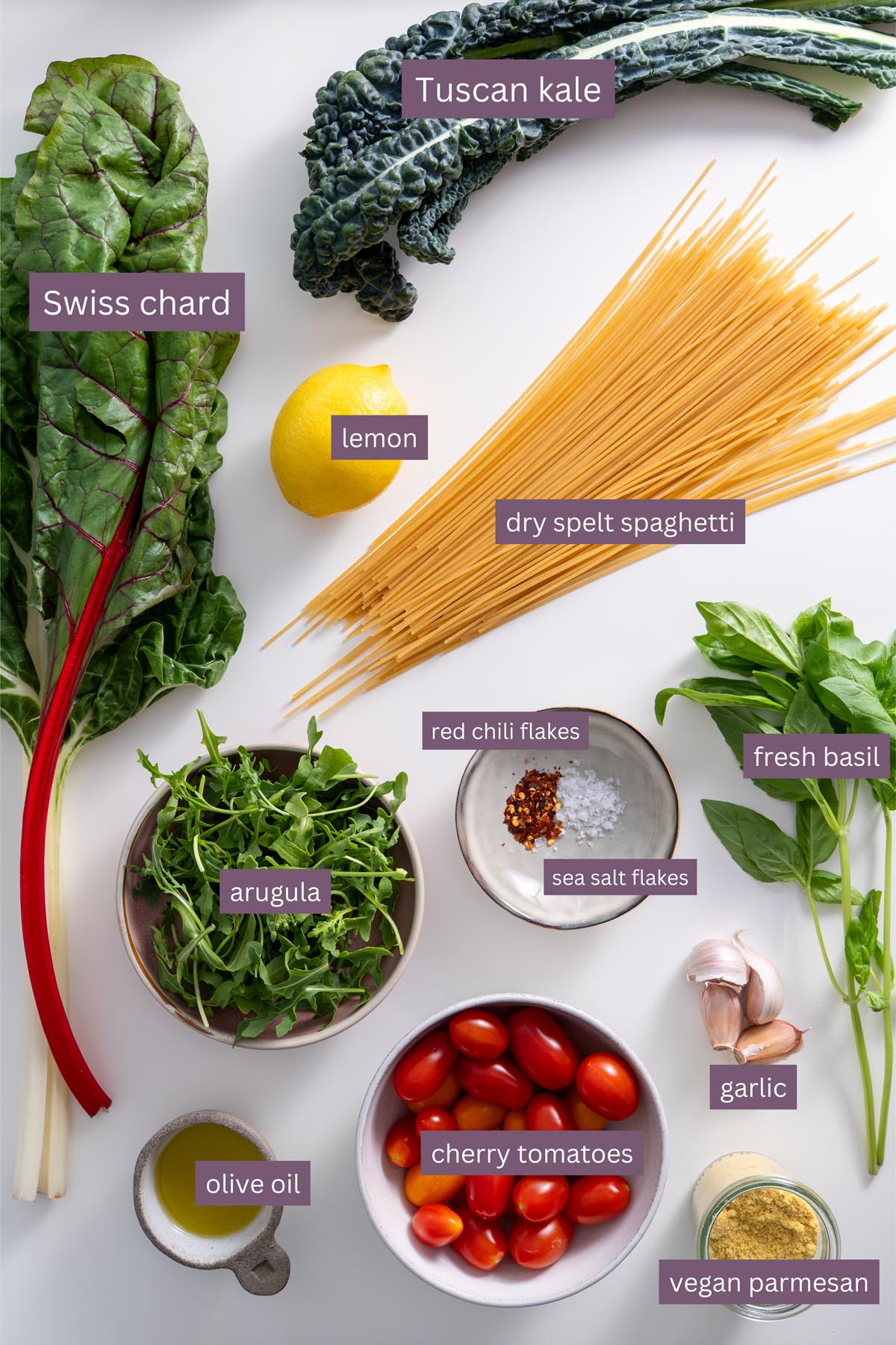 A vibrant overhead shot of fresh ingredients for Meghan Markle’s one-pot pasta, including swiss chard, tuscan kale, cherry tomatoes, lemon, spaghetti, fresh basil, and spices.