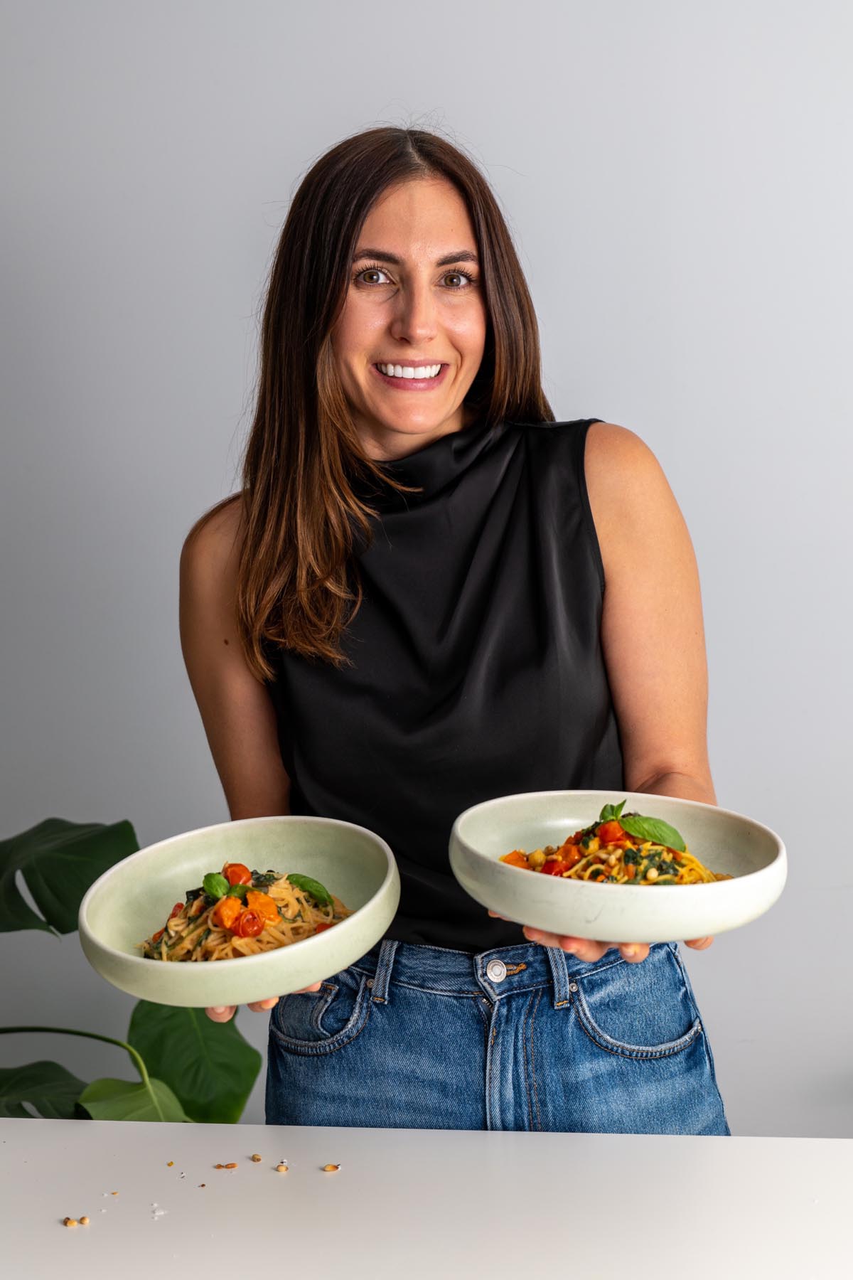 Sarah Cobacho holding two bowls of Meghan Markle’s one-pot pasta, smiling at the camera in a black top and jeans.