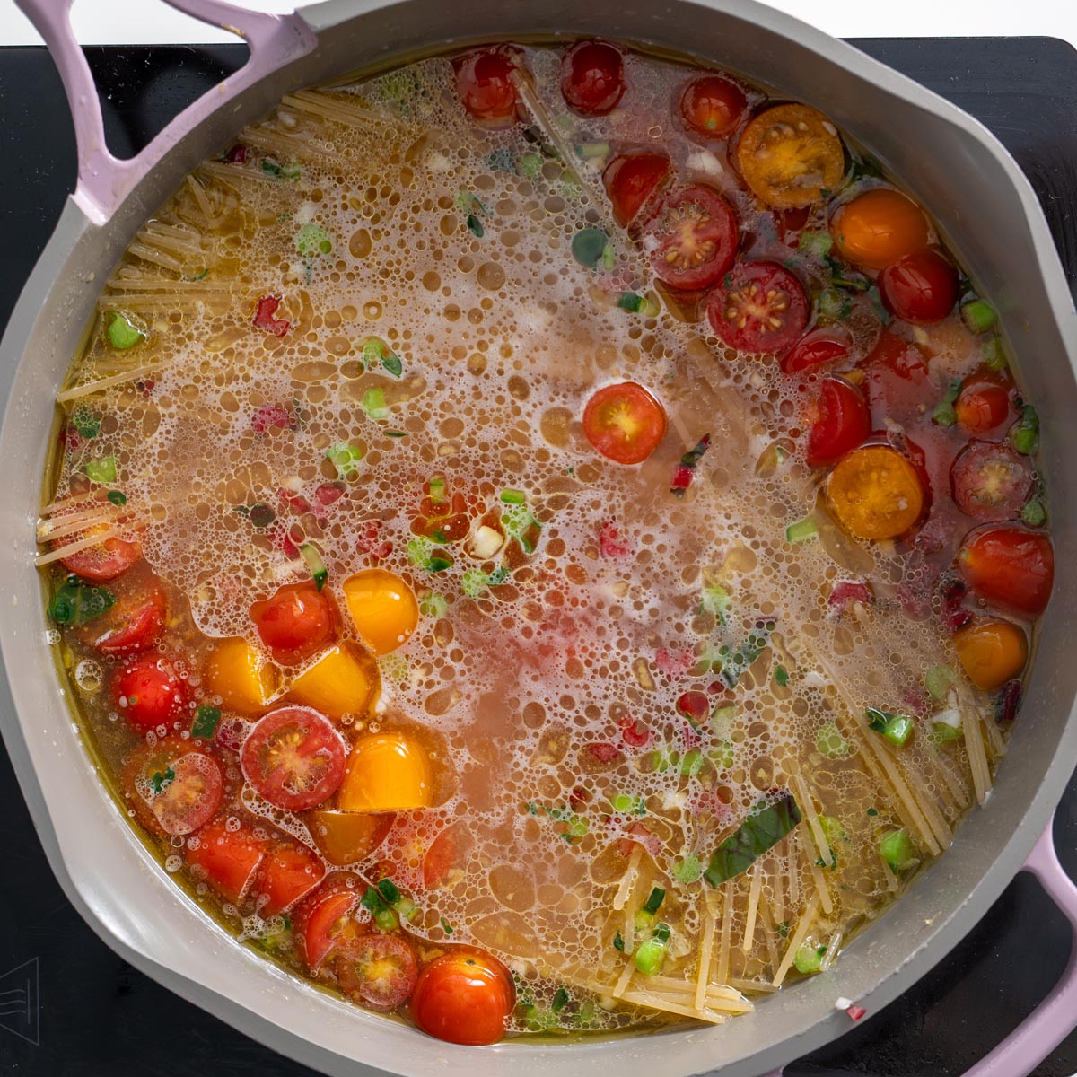 A large pan with boiling broth, cherry tomatoes, spaghetti, and seasonings as the Meghan Markle one-pot pasta begins to cook.