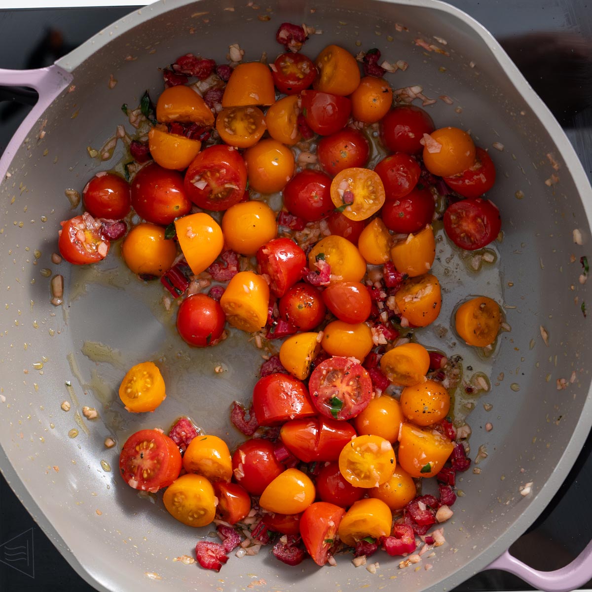 Close-up of cherry tomatoes, garlic, and seasonings being sautéed in a pan for the Meghan Markle one-pot pasta.