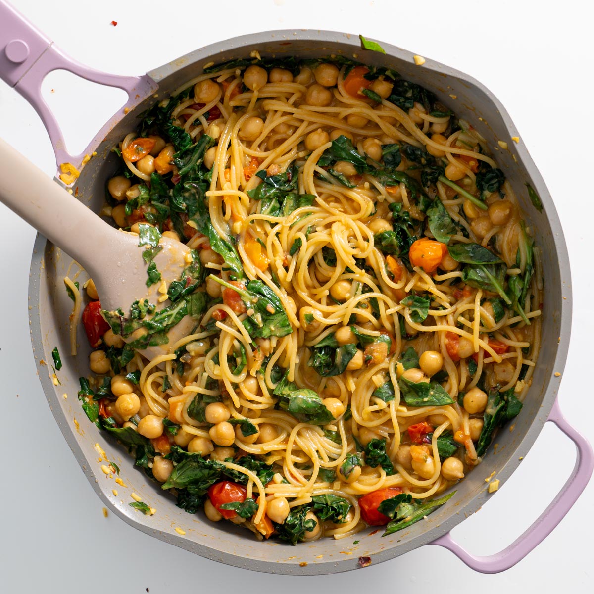 A pot of freshly cooked Meghan Markle one-pot pasta with spaghetti, chickpeas, wilted greens, and a rich tomato sauce being stirred with a spatula.