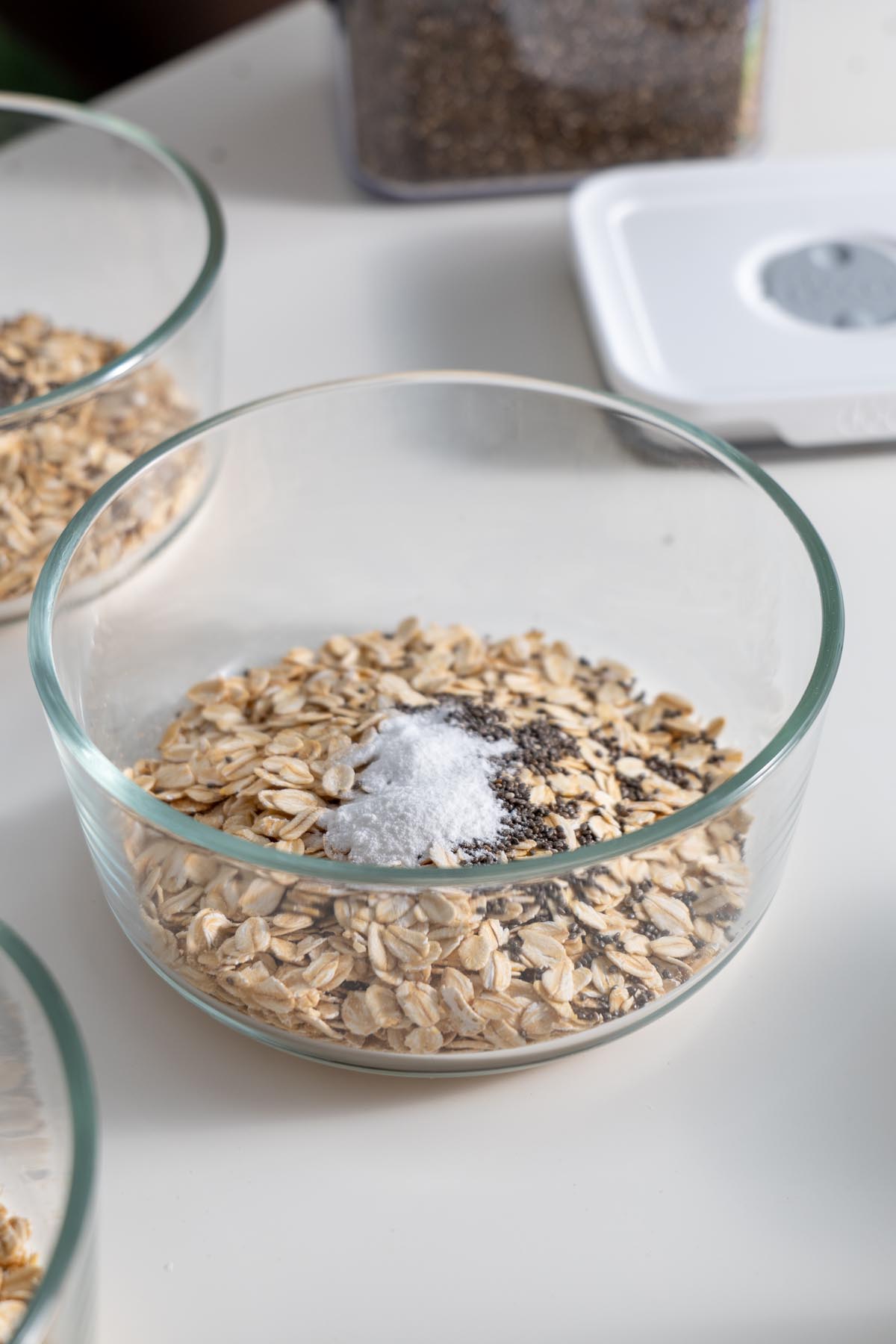 Glass dish with oats, chia seeds, and baking powder before mixing, sitting on a kitchen counter