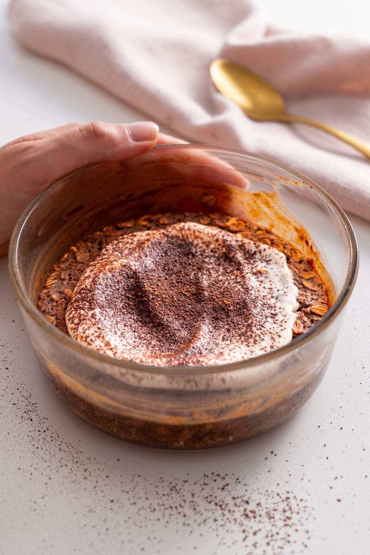 Sarah Cobacho holding a glass dish of tiramisu baked oats, topped with yogurt and cacao powder