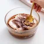 A spoon scooping a bite of tiramisu baked oats from a glass dish