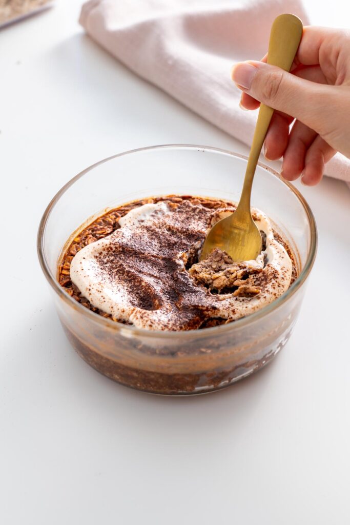 A spoon scooping a bite of tiramisu baked oats from a glass dish