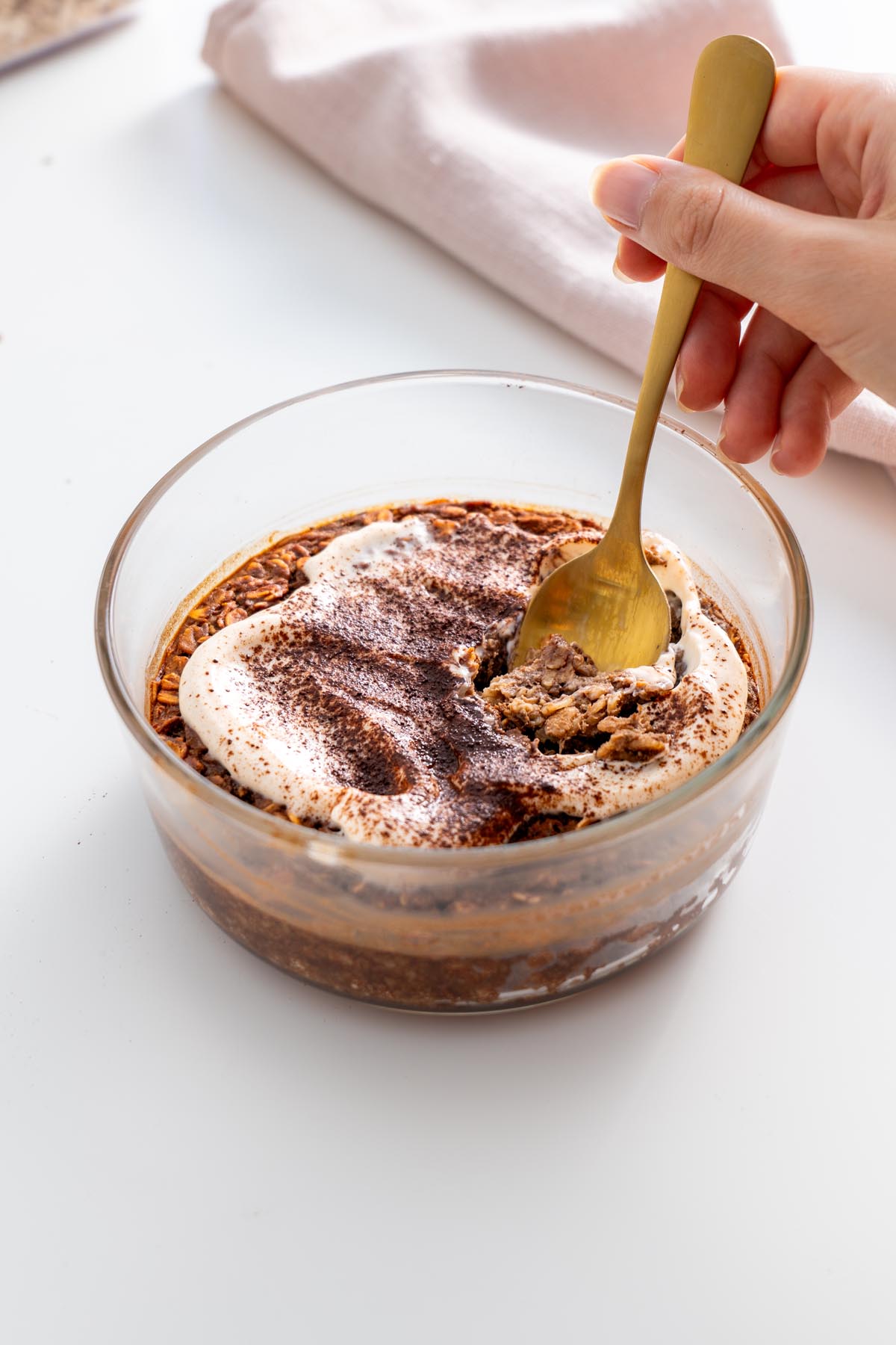 A spoon scooping a bite of tiramisu baked oats from a glass dish