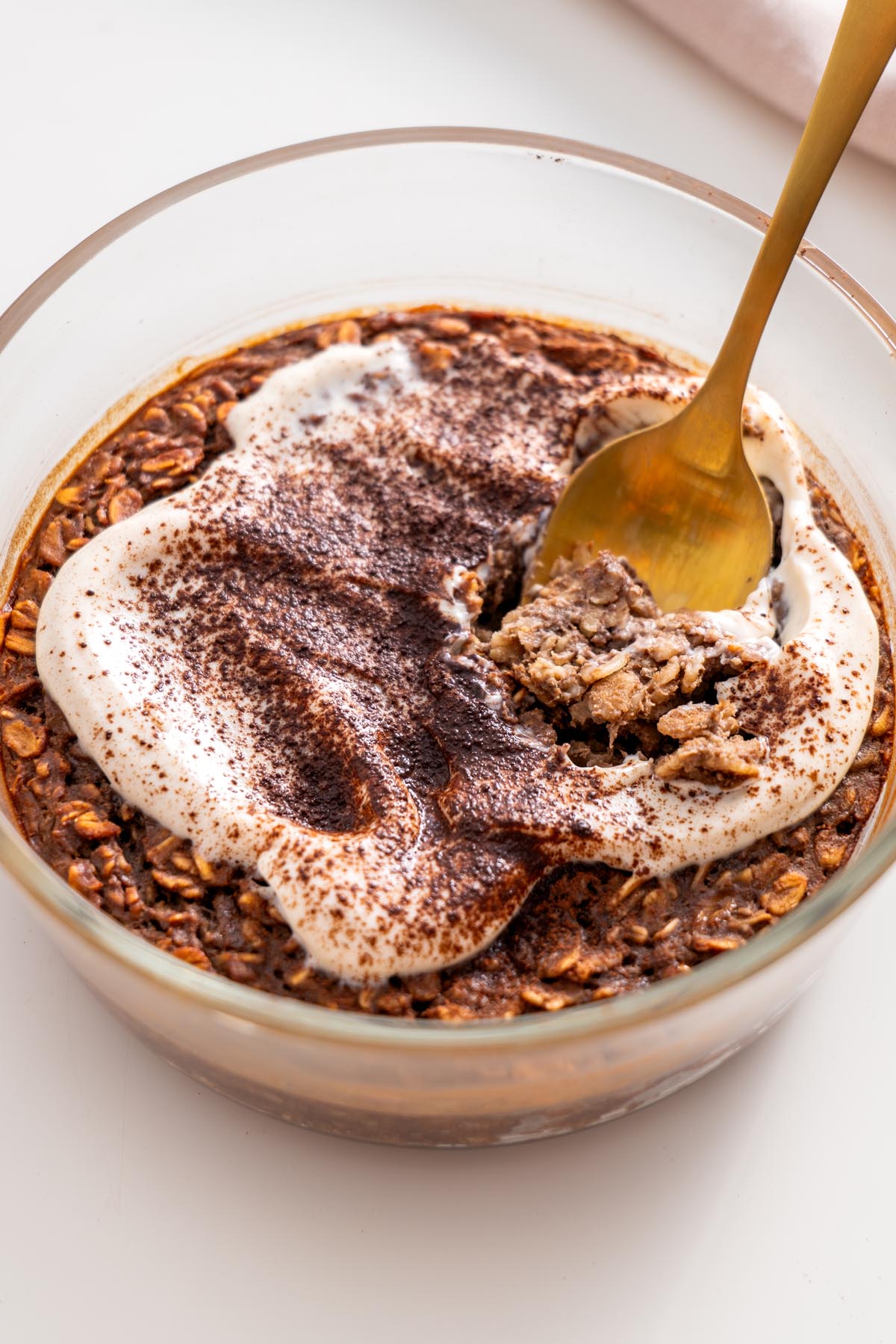 Close-up of baked oats topped with yogurt and cacao powder, with a spoonful being lifted